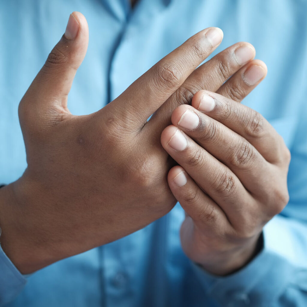 A man in a blue shirt rubbing his hands together, feeling his joints.